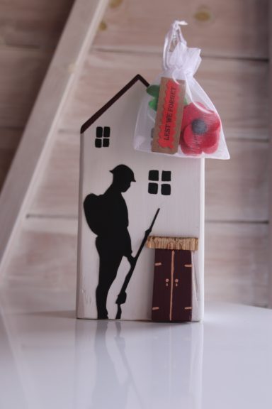Lest We Forget Silhouette of a soldier beside a small house, with a bag of poppies attached.