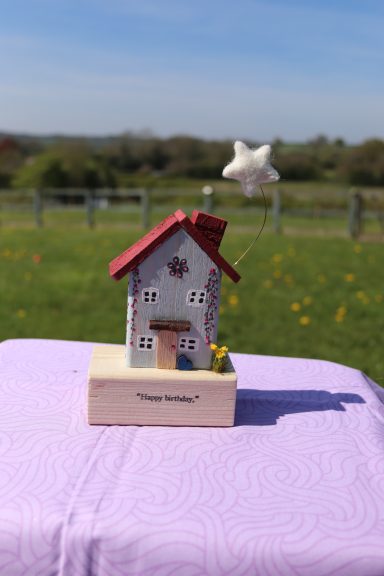 Star Above A decorative miniature house on a wooden base with a flower, set in a grassy field.